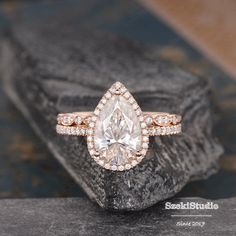 an engagement ring with a pear shaped diamond surrounded by smaller round diamonds on a rock