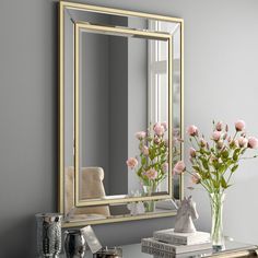 a mirror sitting on top of a table next to a vase filled with flowers