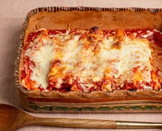 a casserole dish with cheese and sauce in it next to two wooden spoons