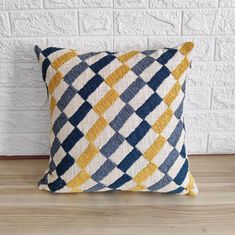 a blue, yellow and white pillow sitting on top of a wooden floor next to a brick wall