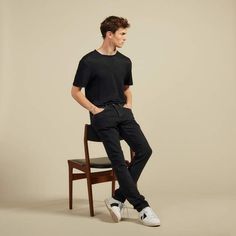 a young man is sitting on a chair and posing for the camera with his hands in his pockets