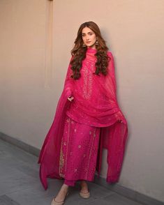 a woman in a pink outfit leaning against a wall