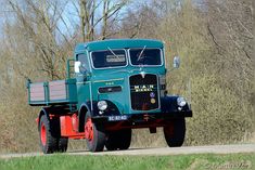 an old green truck driving down a road next to tall grass and tree's