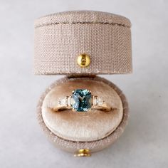 an engagement ring with a blue topaz surrounded by two diamonds in a velvet box