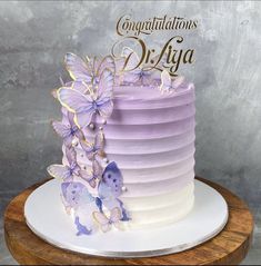 a purple cake with butterflies on top and congratulations written in gold lettering, sitting on a wooden platter