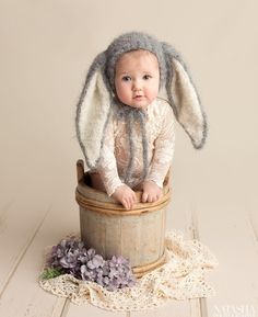 a baby is sitting in a bucket with a bunny hat on it's head