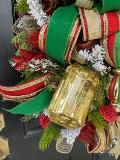 a christmas wreath decorated with green, red and gold ribbons and an emerald stone ornament