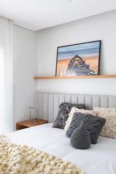 a white bed topped with lots of pillows next to a painting on top of a wall