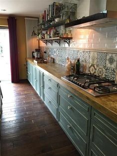 a kitchen with green cabinets and tile backsplash, wood flooring and open shelves