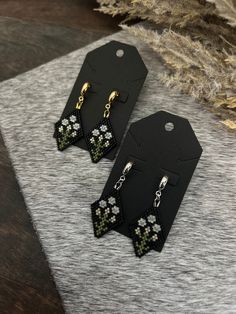 two black and white earrings on top of a gray table next to some dried plants