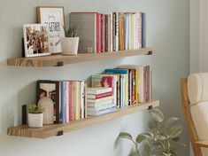 two wooden shelves filled with books next to a white chair and potted plant on the wall