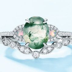 an oval shaped green and white ring with leaves on the side, surrounded by diamonds