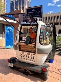 a man is sitting in the back of a small car with a coffee cart attached to it