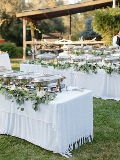 an outdoor table set up with white linens and greenery on it for a wedding reception