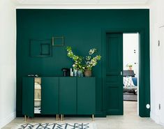 a living room with dark green walls and white flooring, plants in vases on the cabinet