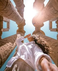 a woman is standing in front of some pillars and looking up at the sky with her hands on her hips