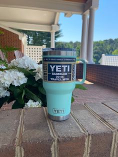 a yeti coffee cup sitting on top of a brick wall next to white flowers