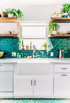 a kitchen with green brick backsplash and white cabinets, potted plants on the window sill