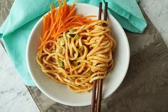 a bowl filled with noodles and carrots next to chopsticks on a table