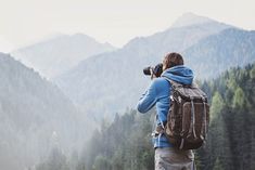 a person with a backpack and camera taking pictures in front of some trees on a mountain