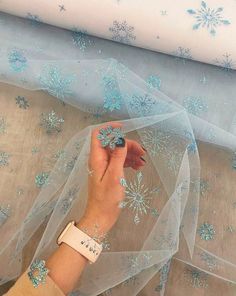 a woman's hand is touching the sheer fabric with blue snowflakes on it