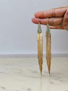 a pair of gold and green earrings on a marble table