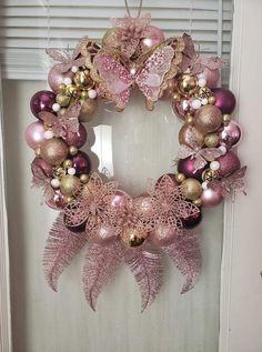 a wreath with pink and gold ornaments hanging from the front door, on a window sill