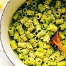 a wooden spoon in a pot filled with pesto pasta