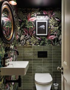 a toilet and sink in a room with wallpapered walls, green tiles and black accents