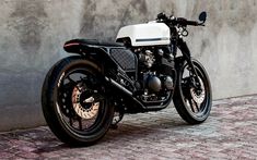 a black and white motorcycle parked next to a gray wall on a brick floored sidewalk