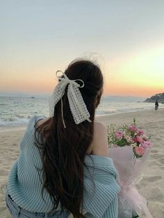 a woman sitting on top of a sandy beach next to the ocean holding a bouquet of flowers