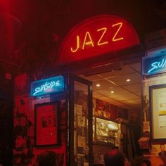 people are sitting at tables in front of a jazz bar with neon signs on the doors