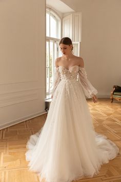 a woman in a white wedding dress standing on a wooden floor with an open window