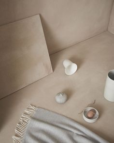 a blanket, vases and an egg sit on a beige couch next to each other