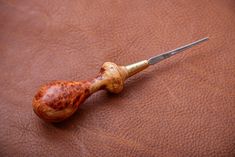 a wooden pipe with a metal handle on a brown leather surface, next to a pair of scissors