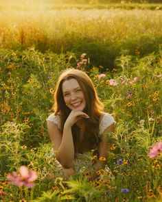 a woman is sitting in the middle of a field with wildflowers and grass