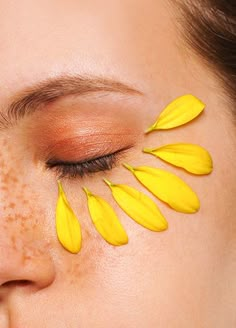 a woman's face with yellow petals painted on her cheek and the eyes are closed