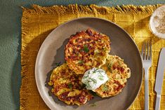 three crab cakes on a plate with a fork and spoon next to it, sitting on a yellow place mat