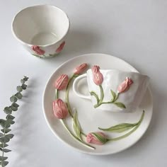 a white plate topped with pink flowers next to a cup and saucer on top of a table