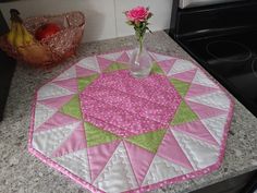 a pink and green quilted table top with a vase filled with flowers on it