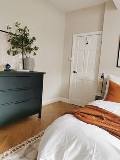 a bedroom with a bed, dresser and potted plant