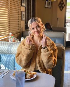 a woman sitting at a table with food in front of her and holding two fingers up to her face