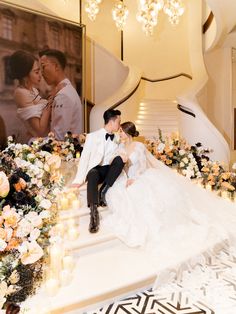 a bride and groom sitting on the stairs in front of a staircase decorated with flowers