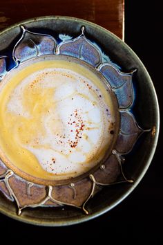 there is a cup of coffee in the bowl on top of a wooden table with a spoon