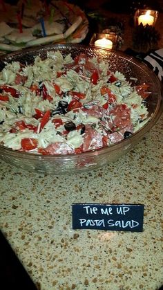 a table topped with a bowl filled with food next to two candles and a sign that says the me up pasta salad