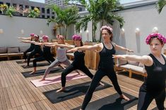 a group of women doing yoga on top of a wooden floor with palm trees in the background