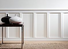 two vases sitting on top of a table in front of a white paneled wall