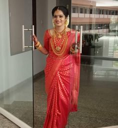 a woman in a red and gold sari is standing by a glass door with her hand on the handle