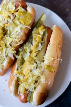 two hot dogs on buns covered in sauerkraut and relish sitting on a white plate