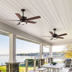 a porch with ceiling fans and table on the front porch next to water in the background